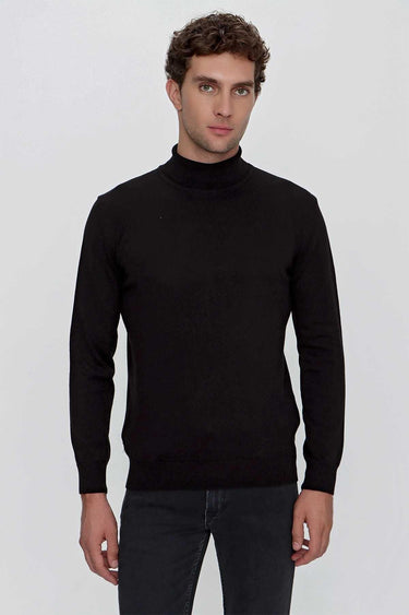 Man wearing a black turtleneck sweater and dark jeans against a plain background