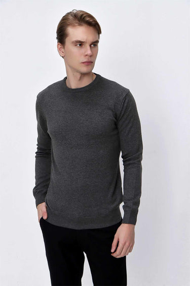 Man wearing a dark grey crew neck knit sweater and black trousers, studio background