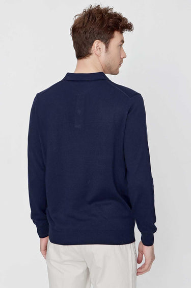 Back view of man wearing a navy blue long sleeve polo shirt with white trousers