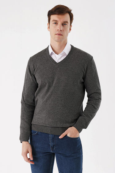 Man wearing a dark grey V-neck sweater over white shirt and blue jeans, front view