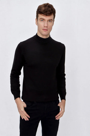 Man wearing black mock-neck sweater and black pants, standing against white background