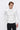 Man wearing a white long sleeve mock neck sweater and dark trousers against plain background