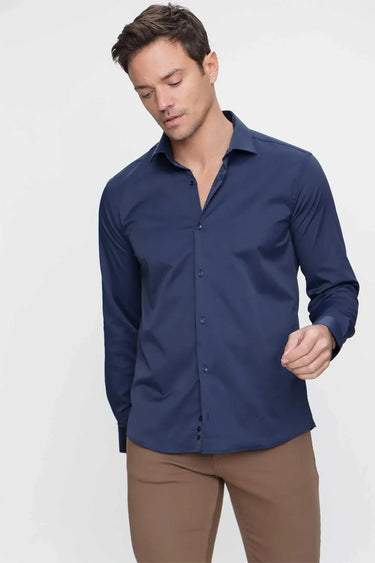 Man wearing a navy blue slim fit dress shirt and brown trousers on a plain background