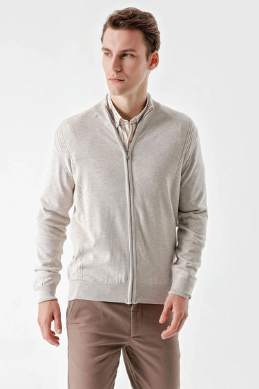 Man wearing a beige jacquard zip-up cardigan with ribbed details and brown trousers.