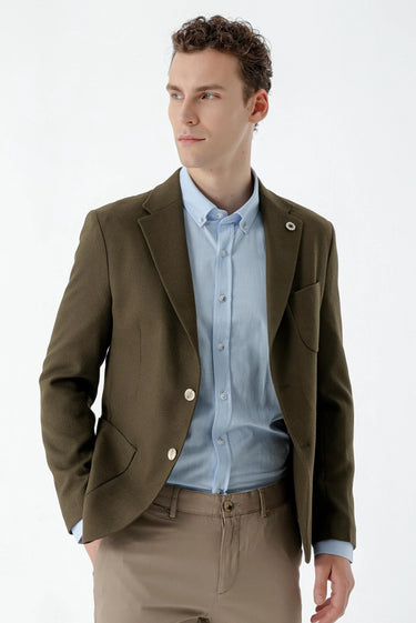 Man wearing khaki slim fit woven blazer, light blue shirt, and beige trousers