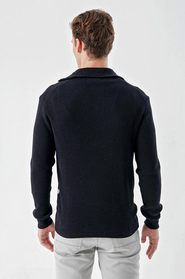 Back view of man wearing navy blue ribbed knit sweater and light grey jeans