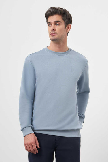 Man wearing a light blue crew neck sweatshirt with long sleeves and dark trousers.