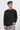 Man wearing black crew neck sweatshirt and light grey pants on white background