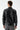 Man wearing a black faux leather jacket and grey jeans, back view
