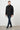 Man wearing a black snap-button jacket with pockets and navy trousers, casual look