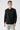 Man wearing black long sleeve polo shirt and light grey jeans, white background