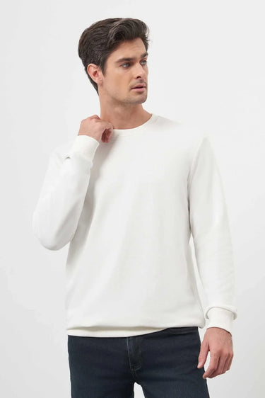 Man wearing a white crew neck long sleeve t-shirt with dark jeans, plain background