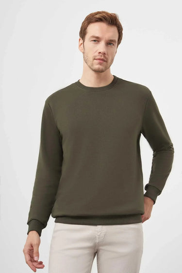 Man wearing khaki crew neck long sleeve sweatshirt and light pants on white background