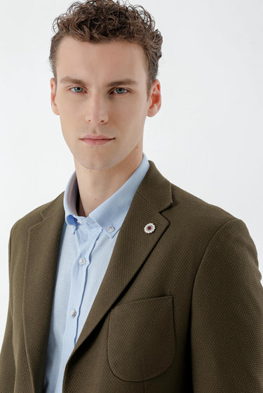 Man in a khaki slim fit blazer with textured fabric, light blue shirt, and lapel pin