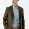 Man wearing khaki slim fit woven blazer, light blue shirt, and beige trousers