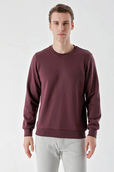 Man wearing a plain burgundy crew neck sweatshirt and light gray jeans on white background