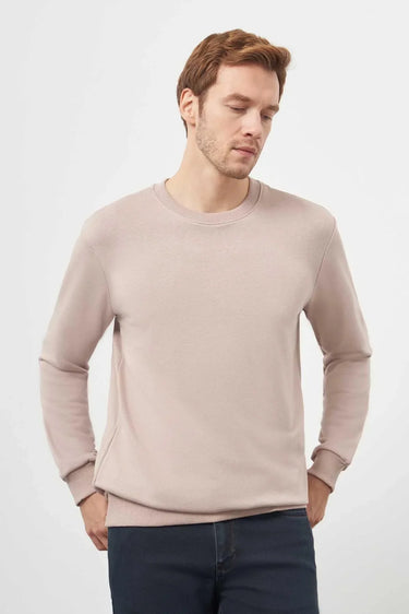 Man wearing a light beige crew neck sweatshirt and dark jeans on white background